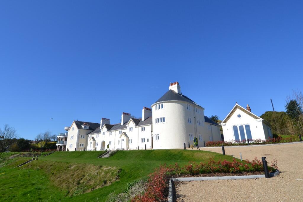 Large white building with a round central tower, chimneys, and multiple pitched roofs, set on green lawns under a clear blue sky, with a gravel driveway in the foreground.