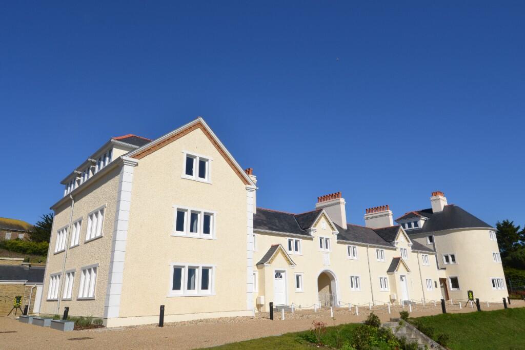 A large, cream-colored apartment building with white trim and chimneys stands under a clear blue sky, surrounded by a gravel path and grassy area.